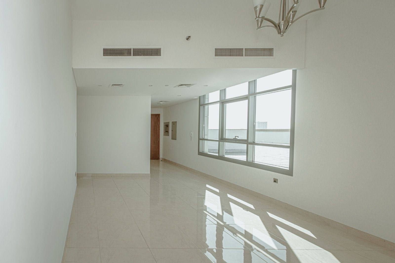 Sala vazia de apartamento novo com janelas amplas e piso claro.